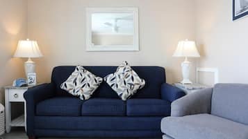 A living room with a dark blue sofa, two patterned throw pillows, a white-framed mirror, and two bedside lamps.