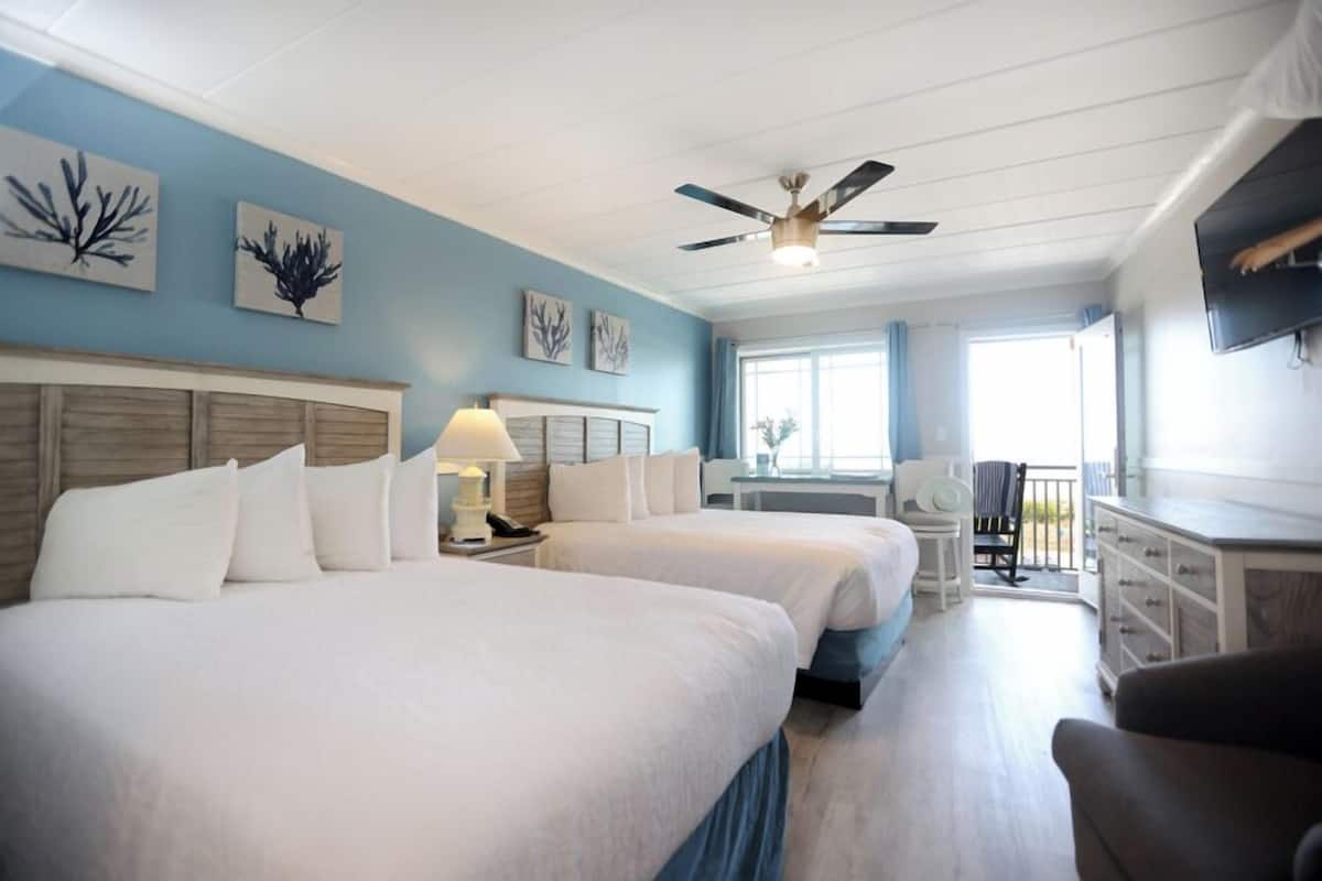 A hotel room with two beds, a desk, a chair, a TV, and artwork on the walls.