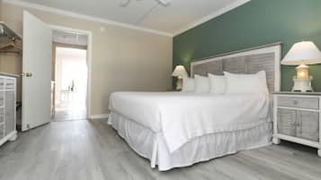 Quarto com cama grande, duas luminárias de cabeceira, cabeceira de madeira e cômoda branca.