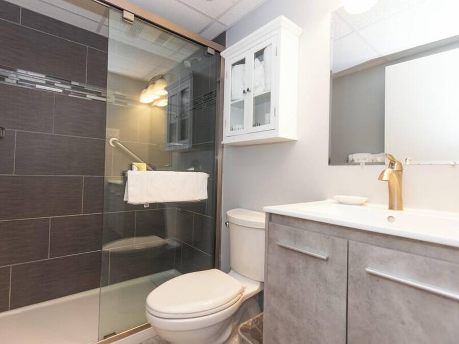 A modern bathroom with a glass shower enclosure, a white toilet, and a vanity with a gold faucet.