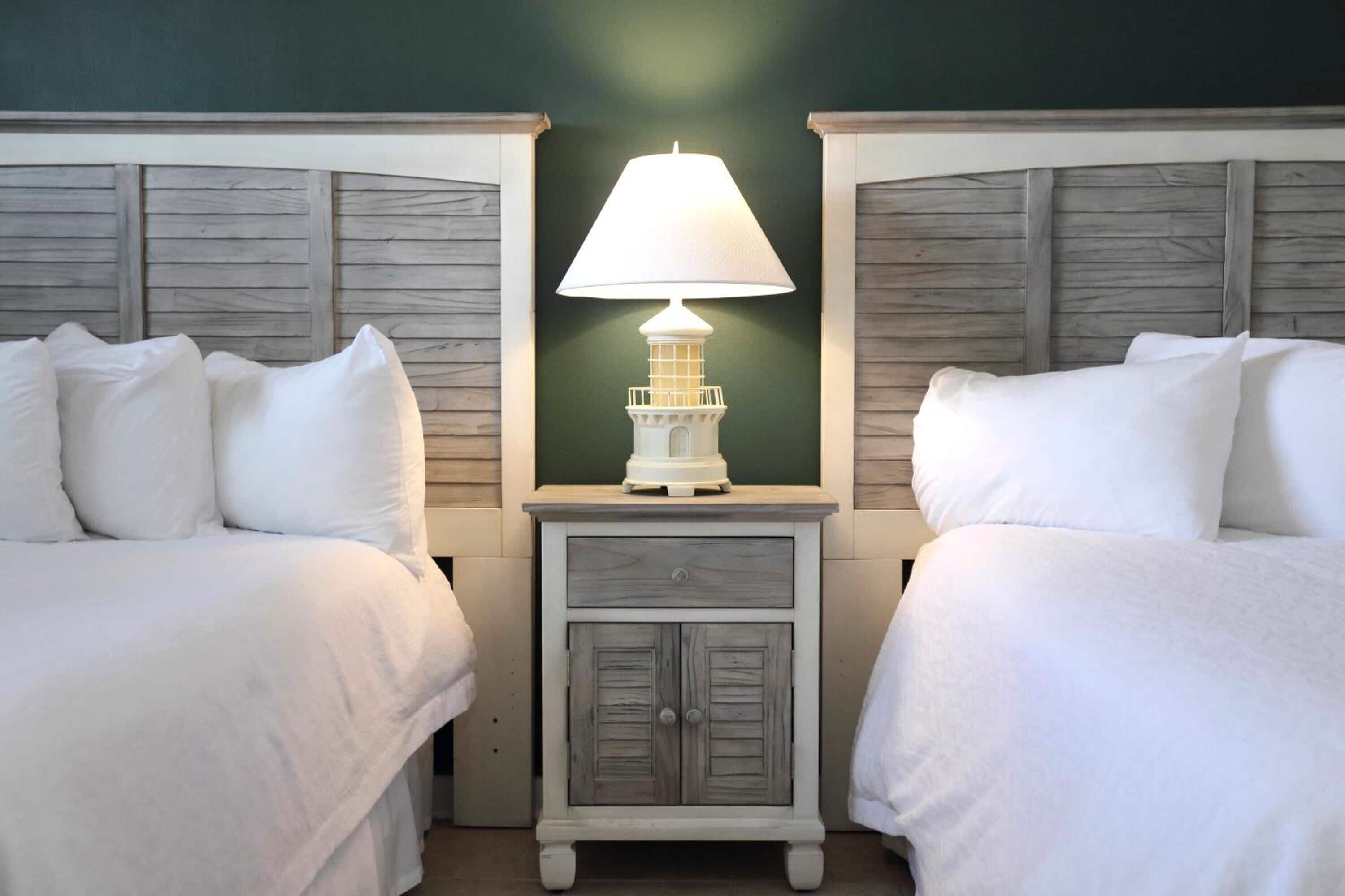 A room with two beds, a nightstand with a lamp, and a small cabinet.