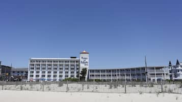 Un hotel frente a la playa con varios pisos, una torre destacada y una playa arenosa al frente.