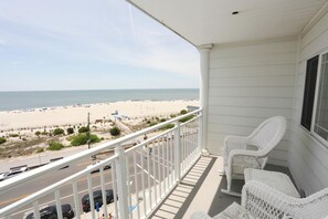 A balcony with white wicker chairs, a view of the beach, and a clear sky.