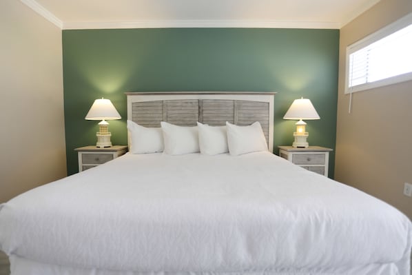 Una cama grande con cabecera de madera, dos mesitas de noche con lámparas y paredes verdes.
