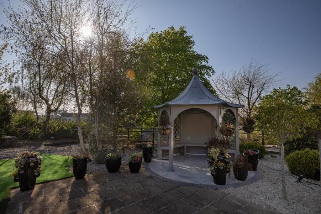 A gazebo with a tiled roof, surrounded by potted plants and a gravel pathway.
