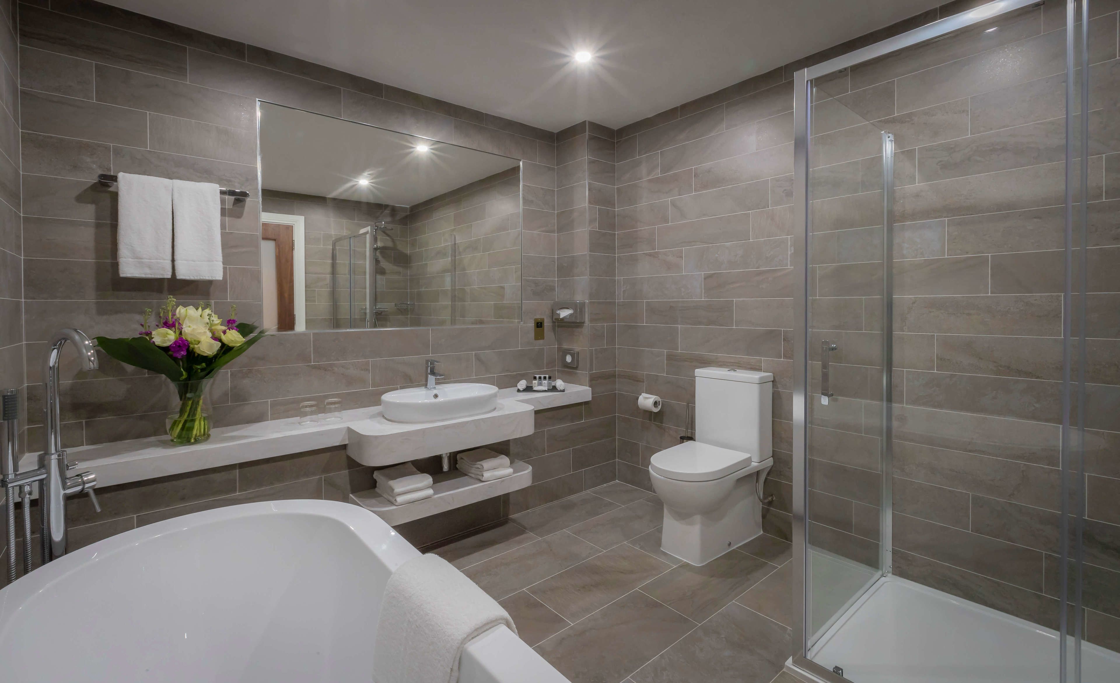 A modern bathroom with a bathtub, two sinks, a toilet, and a glass-enclosed shower.