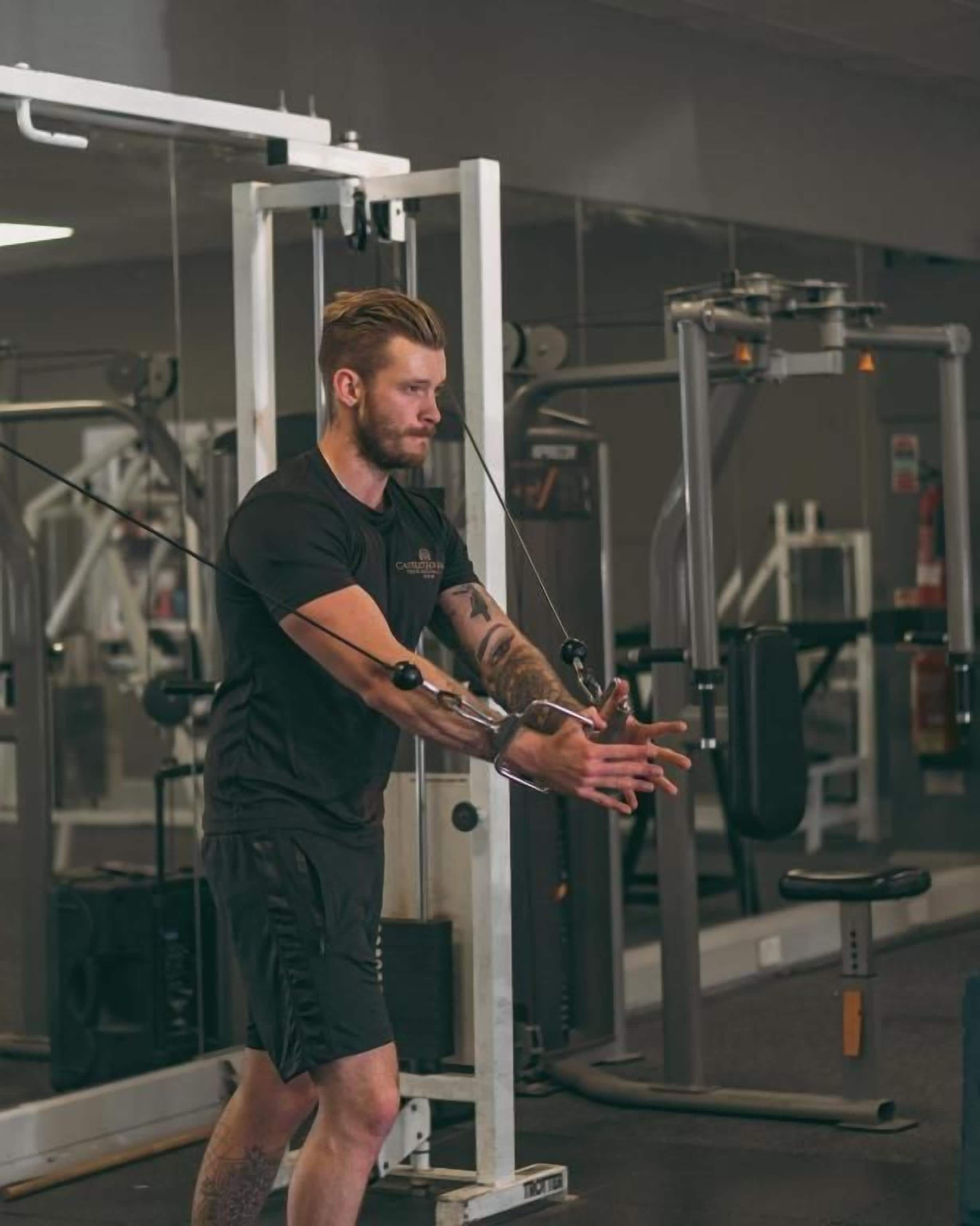Una persona utilizza una macchina per cavi in palestra, circondata da diverse attrezzature per l'allenamento.