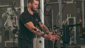 Una persona usando una máquina de poleas en un gimnasio con diverso equipo de ejercicio.