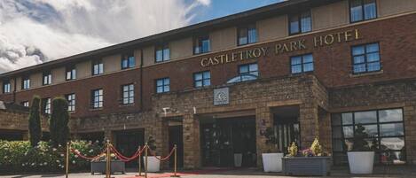 Un hotel con fachada de ladrillo, un letrero con el nombre y una entrada con alfombra roja.