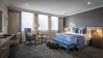 A hotel room with a large bed, a desk with a chair, a small table, and a bench.