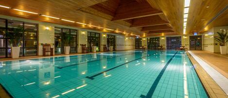 An indoor swimming pool with clear lane markings, wooden ceiling beams, and large windows allowing natural light.