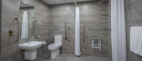 A modern bathroom with a shower, toilet, and sink, featuring grab bars and a wheelchair-accessible bench.