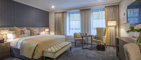 A hotel room with a large bed, a small table, a chair, a bench, and a desk.