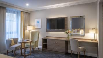 A hotel room with a desk, two chairs, a TV, a mirror, a lamp, and a vase with flowers.