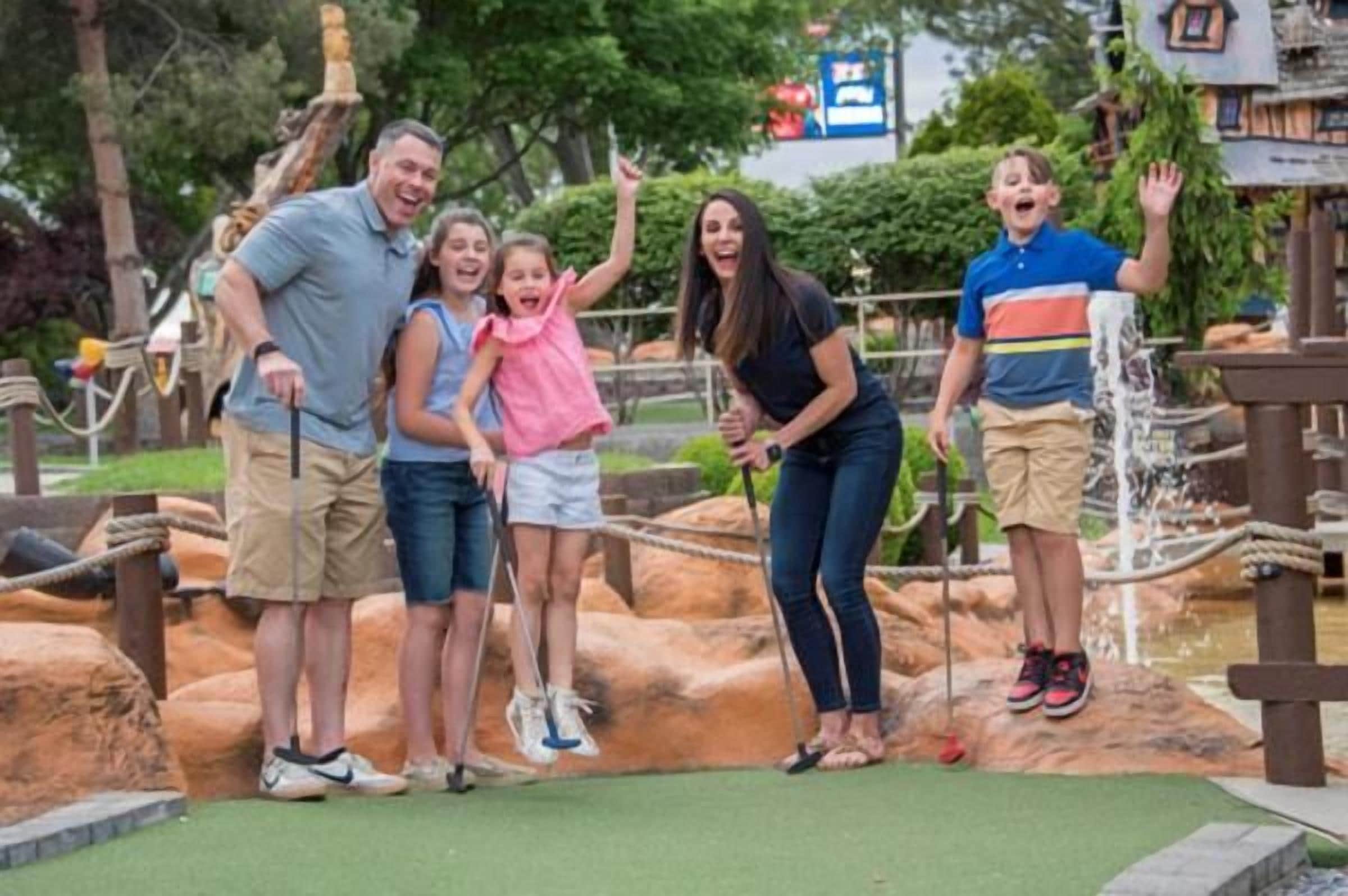 A group of people standing on a play structure with a rope bridge and a water feature.