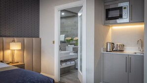 A modern hotel room with a bed, bedside lamp, and a kitchenette with a microwave, kettle, and sink. - Castletroy Park Hotel Suites (Limerick)