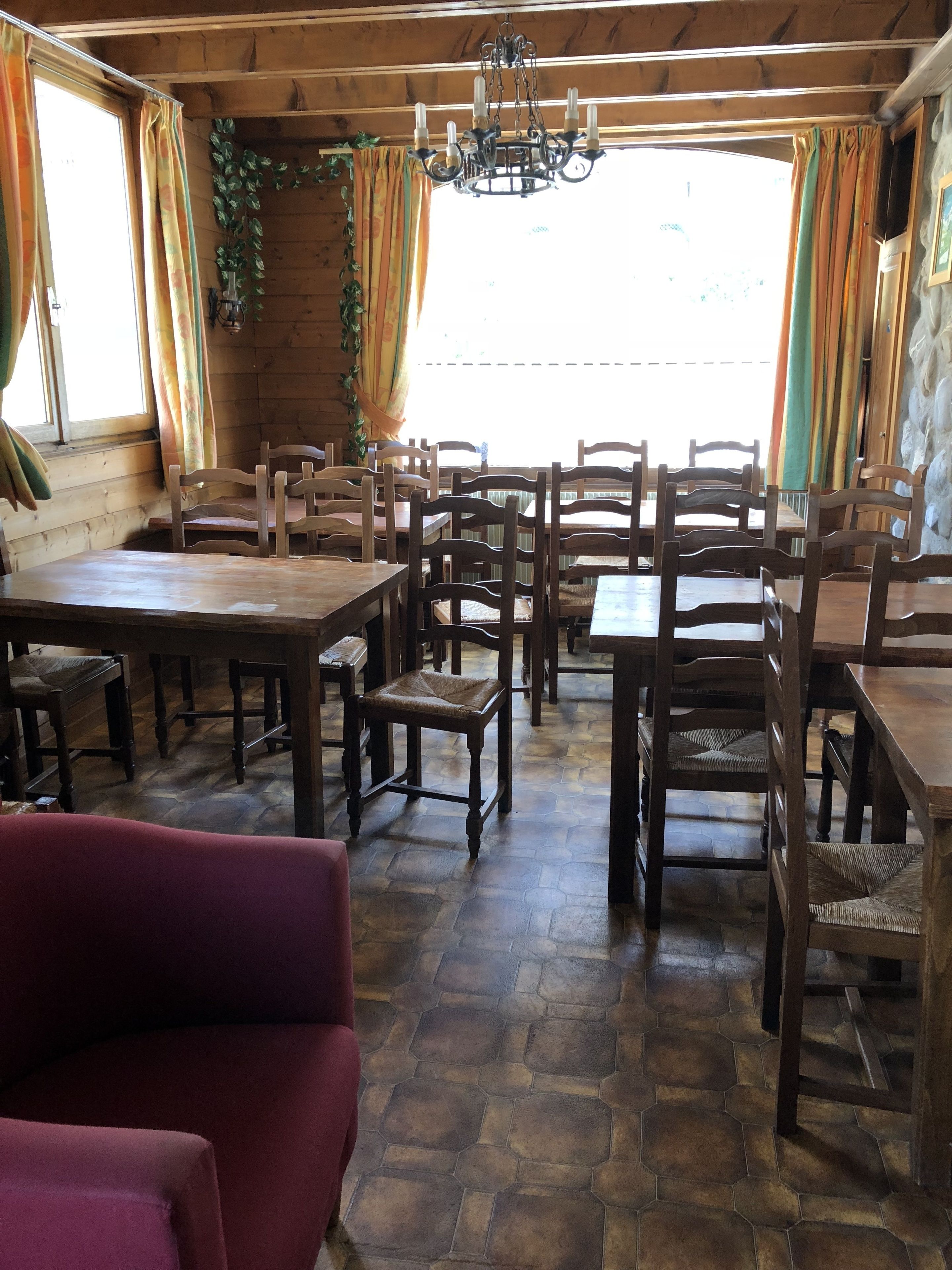 Un coin repas rustique avec des tables et des chaises en bois, un lustre et un sol carrelé en pierre.
