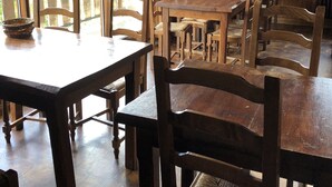 Spiseområde med træborde og stole, store vinduer med gardiner og udsigt til det fri.
