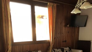 Et hyggeligt opholdsområde med sofa, stole, et lille rundt bord og et fjernsyn monteret på væggen.