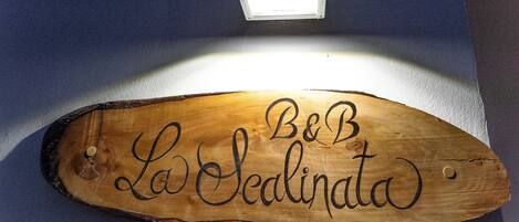 Ein Holzschild mit der eingravierten Aufschrift "B&B La Sedinata", beleuchtet von einer Deckenleuchte.