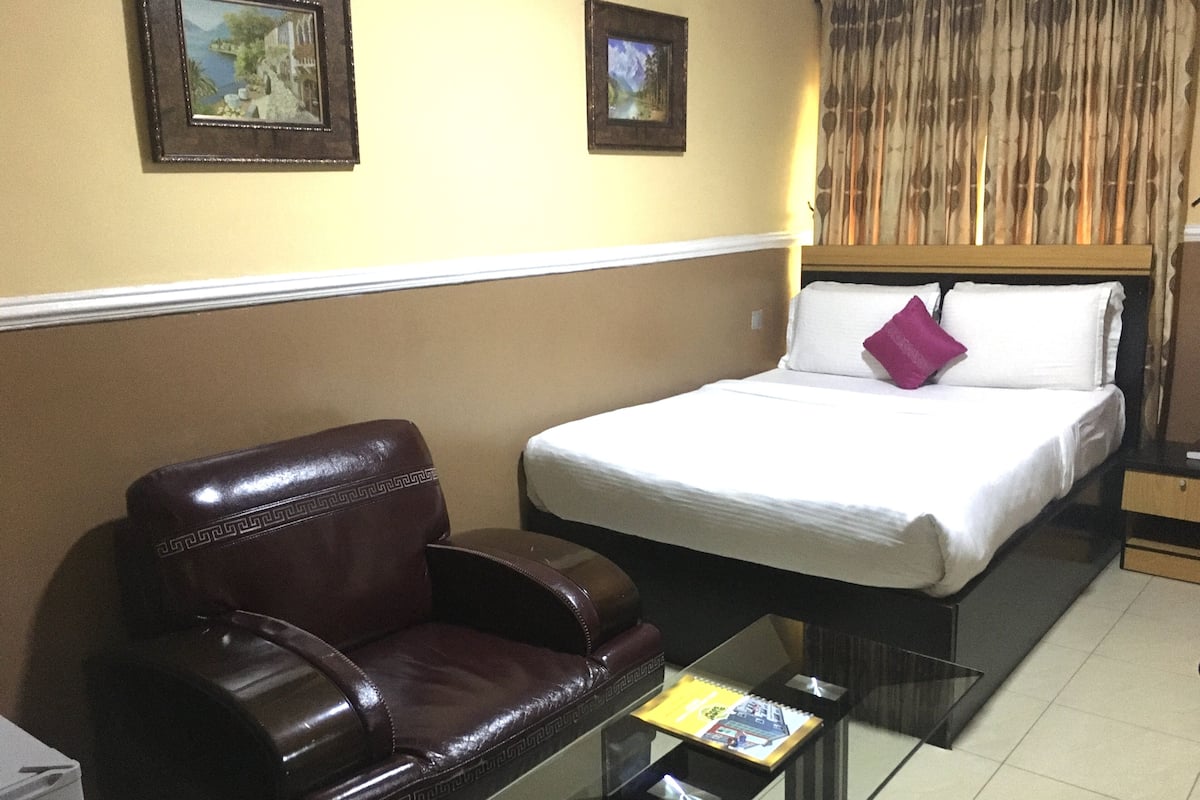 Une chambre d’hôtel avec un lit, un fauteuil en cuir et une petite table sur laquelle se trouve un livre.
