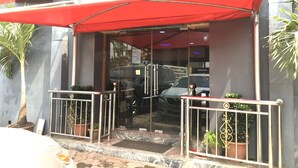 A building entrance with a red awning, glass doors, metal railings, and potted plants. - Sweet Savor Hotels & Suites (Lagos)