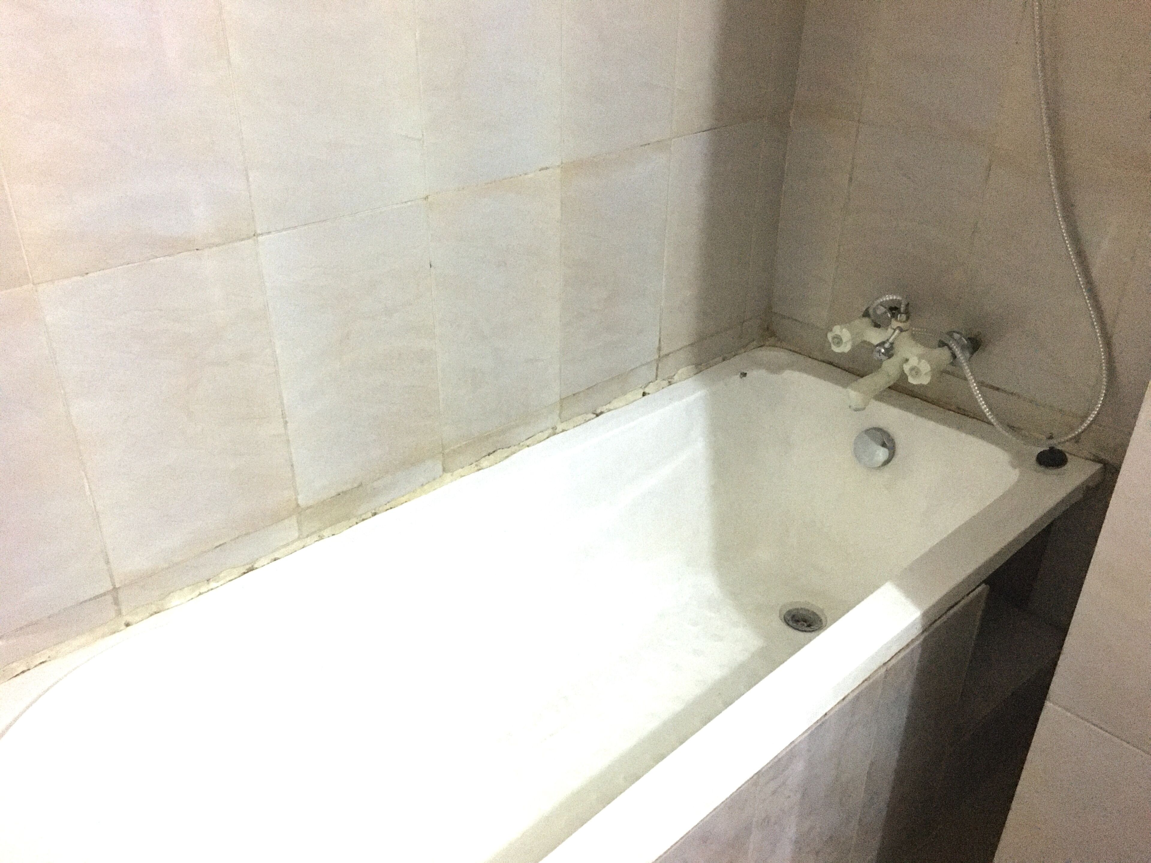 Una bañera estándar con cabezal de ducha y grifo, paredes con azulejos y desagüe.