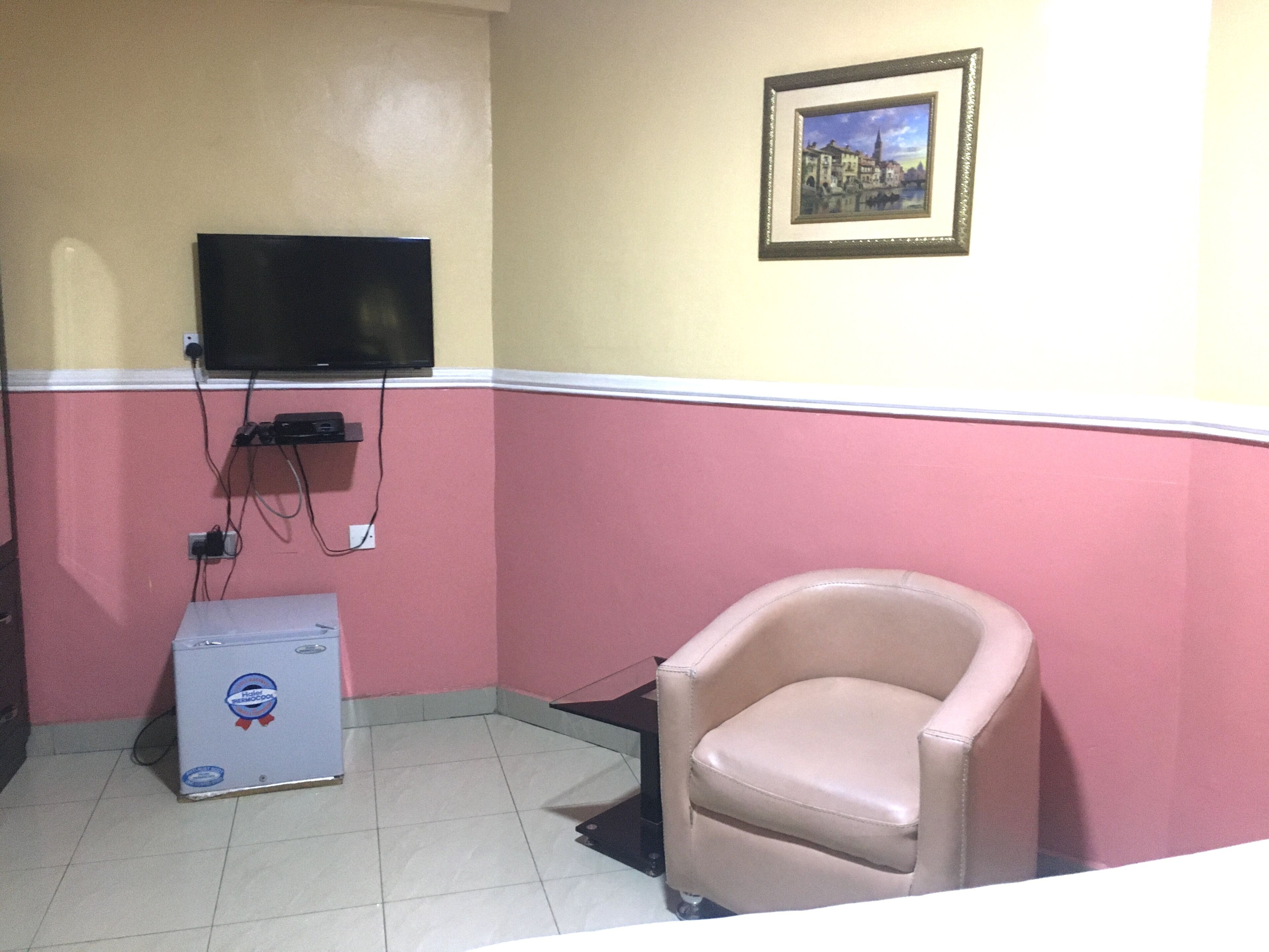 A room with a television mounted on the wall, a small cabinet, a chair, and a framed picture.