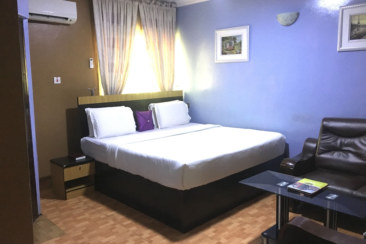 Une chambre d’hôtel équipée d’un lit, d’une chaise, d’une table de chevet, d’un climatiseur et d’une fenêtre avec des rideaux.