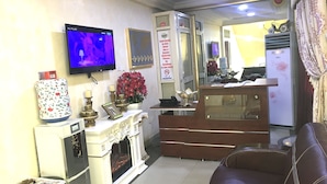 A hotel reception area with a television, a decorative fireplace, a reception desk, and a brown leather sofa. - Sweet Savor Hotels & Suites (Lagos)