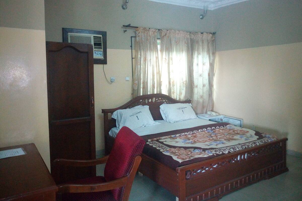 A bedroom with a bed, a wooden chair, a desk, and a wardrobe.
