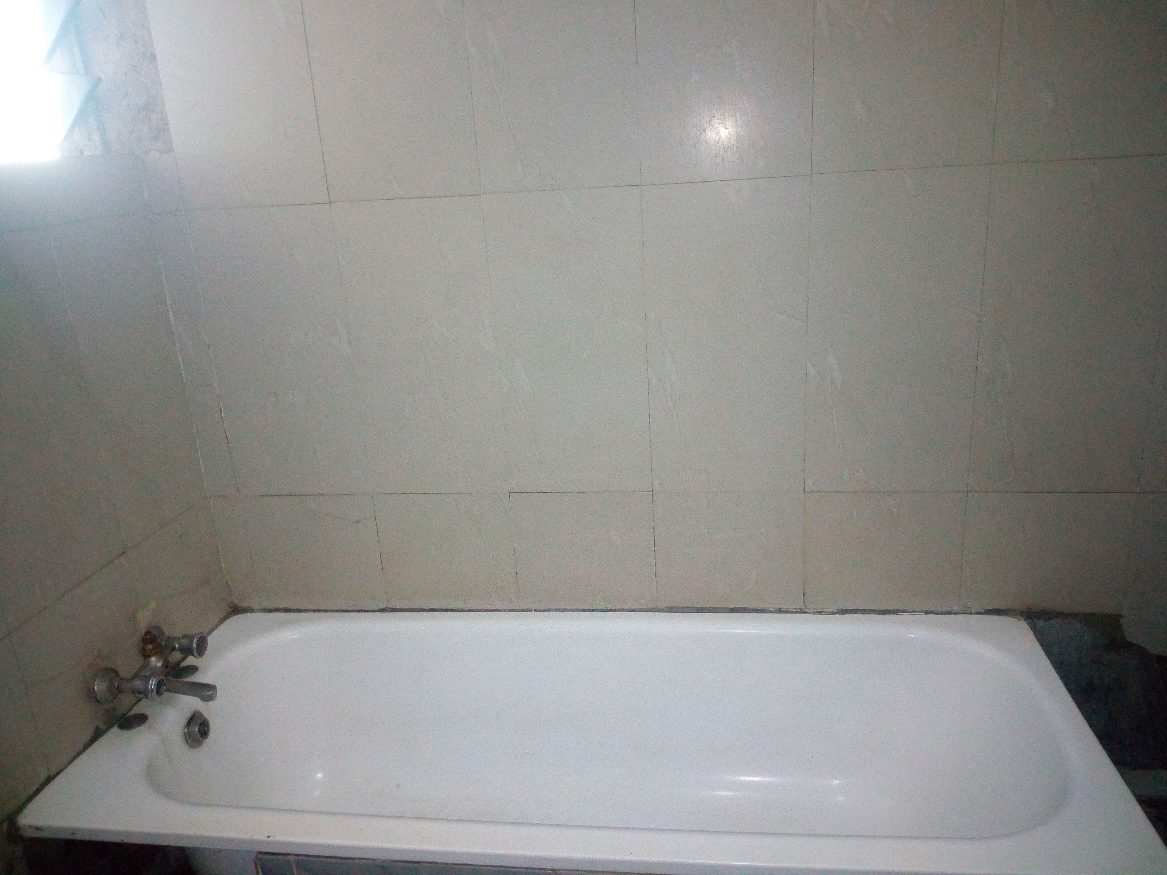 A bathroom with a white bathtub, a visible faucet, and tiled walls.