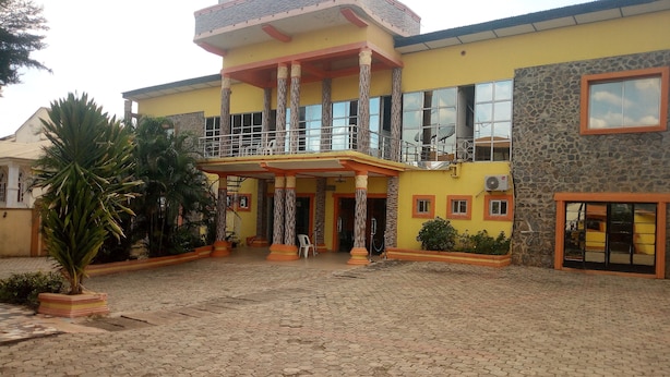 A building with a yellow facade, a covered entrance area, and a paved courtyard. - Sylvia's Place (Ibadan)