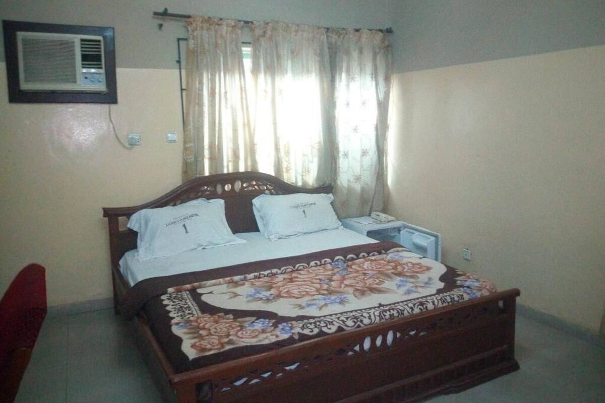 A bedroom with a wooden bed, a nightstand, a wall-mounted air conditioner, and a window with curtains.
