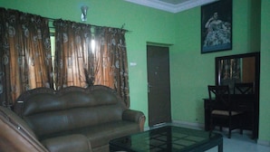 A living room with a brown leather sofa, a glass coffee table, a dark wooden door, and a framed picture on the wall. - Sylvia's Place (Ibadan)