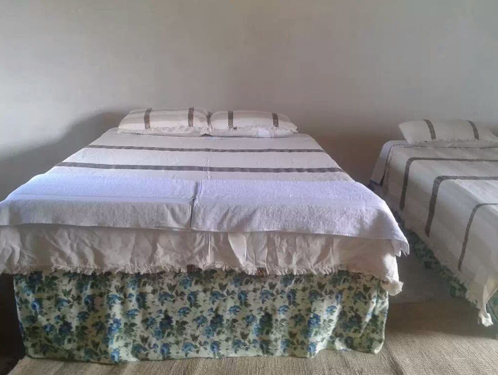 A bed with a floral-patterned skirt, a white duvet, and a striped blanket.