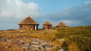Three thatched-roof huts with stone walls, set on a grassy hill with rocky terrain. - Degosach Eco Lodge (Lalibela)