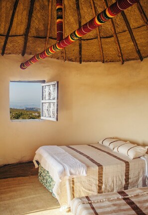 A room with a bed, a window with a view, and a thatched roof. - Degosach Eco Lodge (Lalibela)