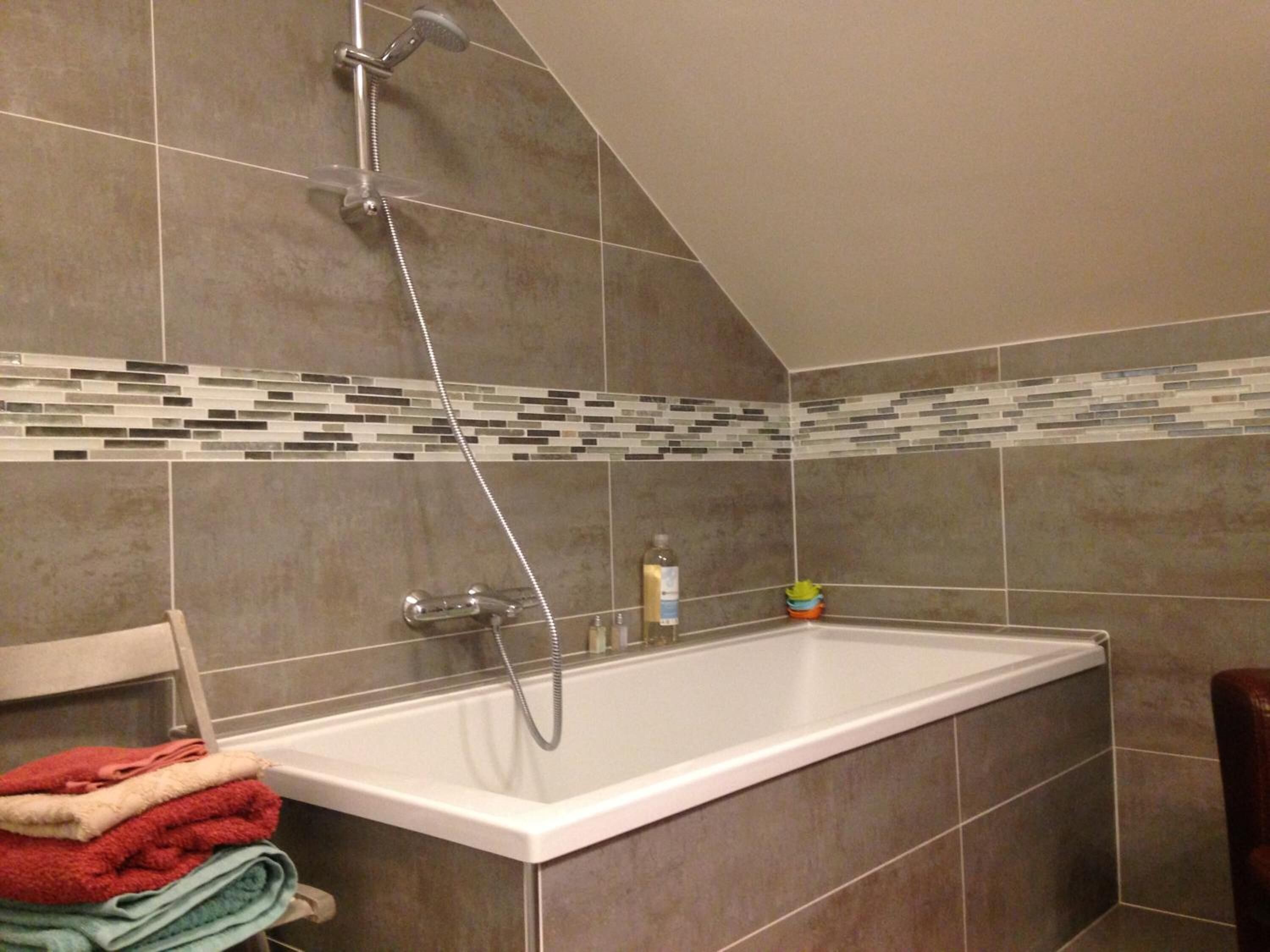Um banheiro com banheira, paredes revestidas de azulejos e chuveiro.
