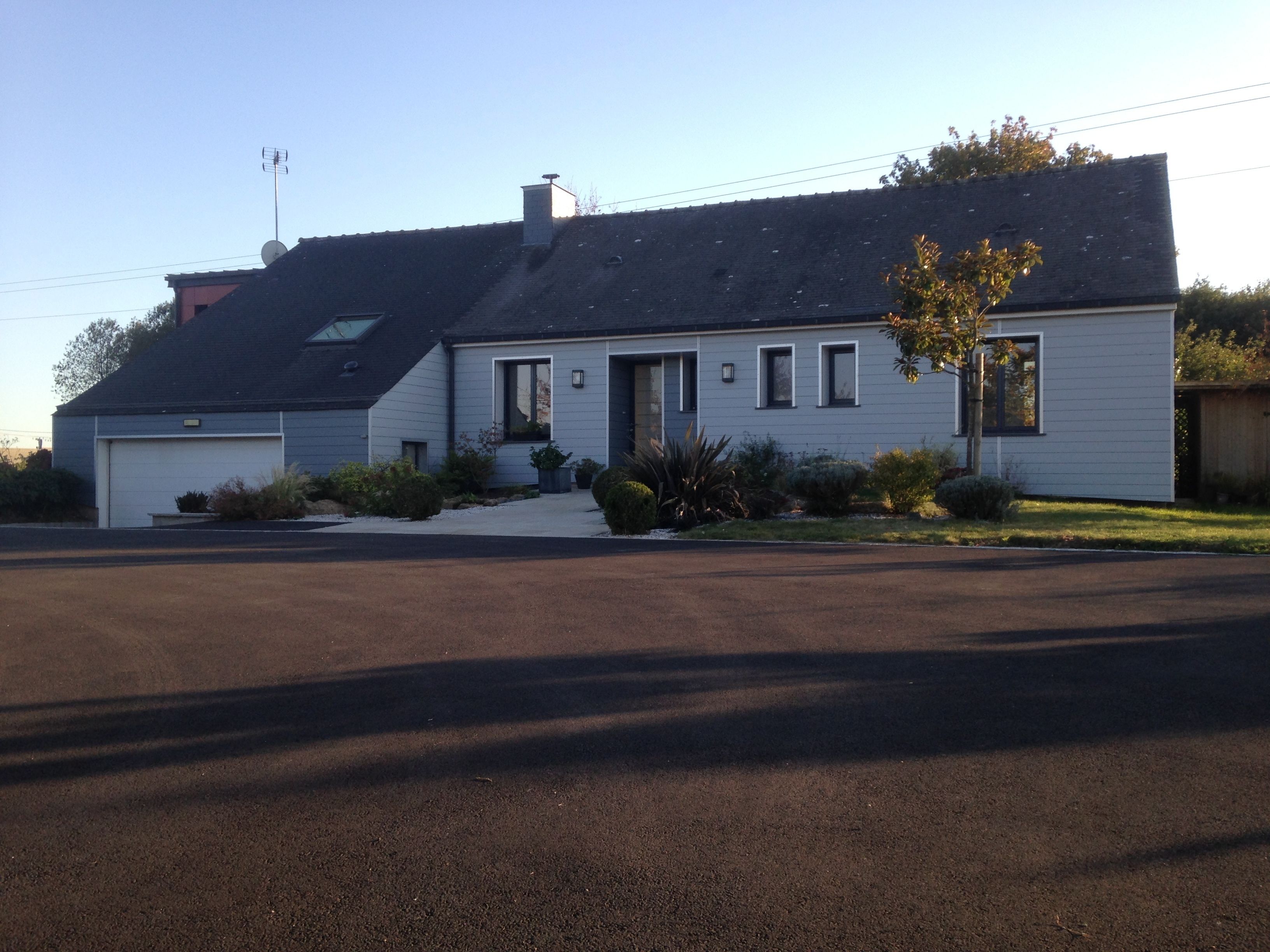 Une maison de plain-pied avec un garage, une allée couverte et un petit jardin devant, agrémenté d’aménagements paysagers.