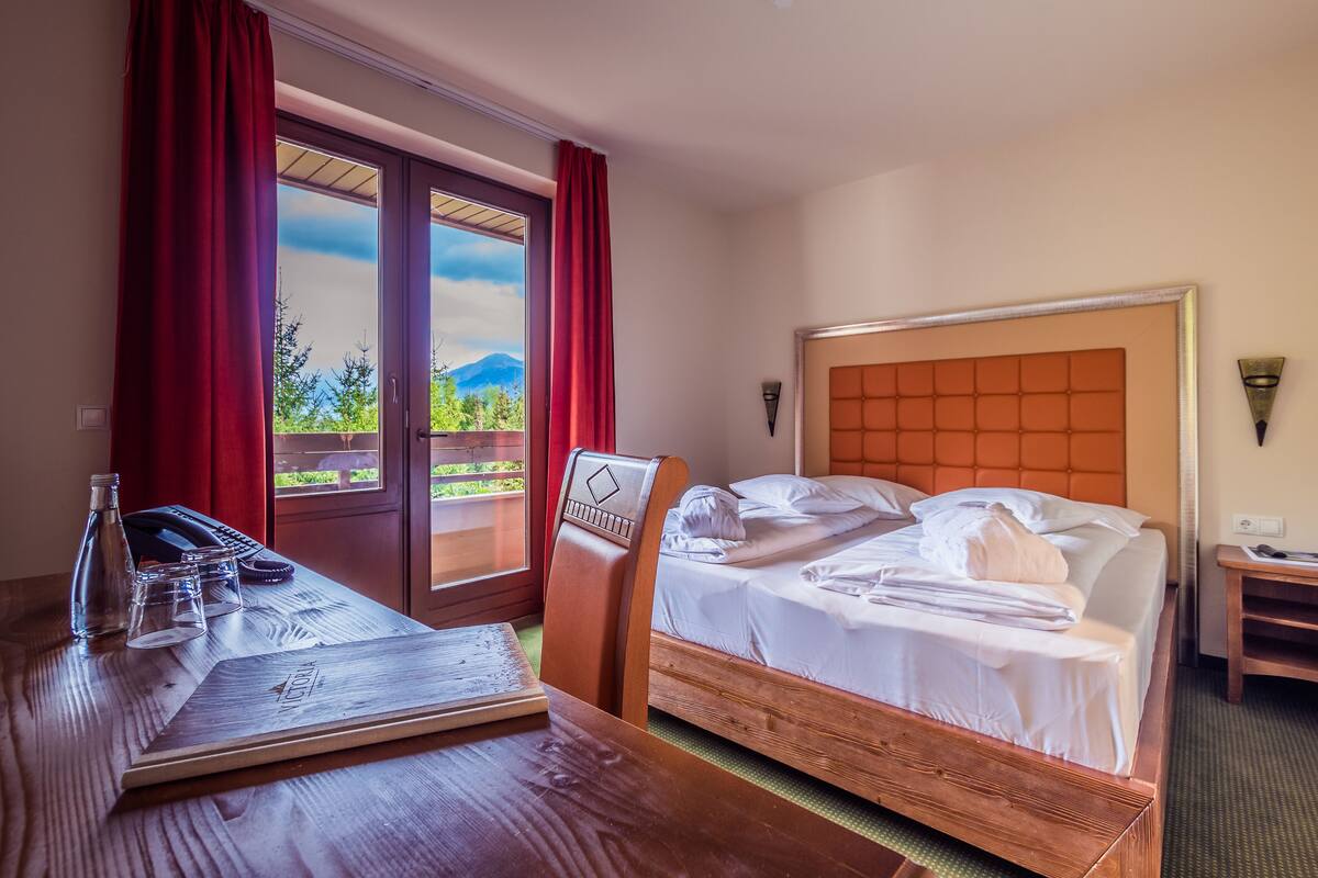 Una habitación de hotel con una cama, un escritorio de madera, un teléfono, vasos y una botella.