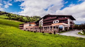 A large, multi-story building with a wooden balcony, set in a lush green landscape with a clear sky. - Hotel Victoria Kaprun (Kaprun)