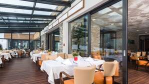 A spacious indoor dining area with multiple tables and chairs, large windows, and a modern architectural design. - Hotel Victoria Kaprun (Kaprun)