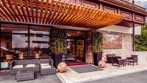 A hotel entrance with a wooden pergola, outdoor seating, and potted plants. - Hotel Victoria Kaprun (Kaprun)