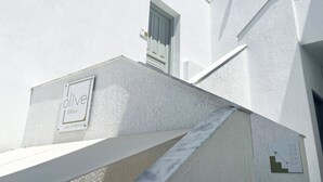 A white building with a sign reading "Olive Milos" and a staircase leading to a door. - Olive Studios (Milos)