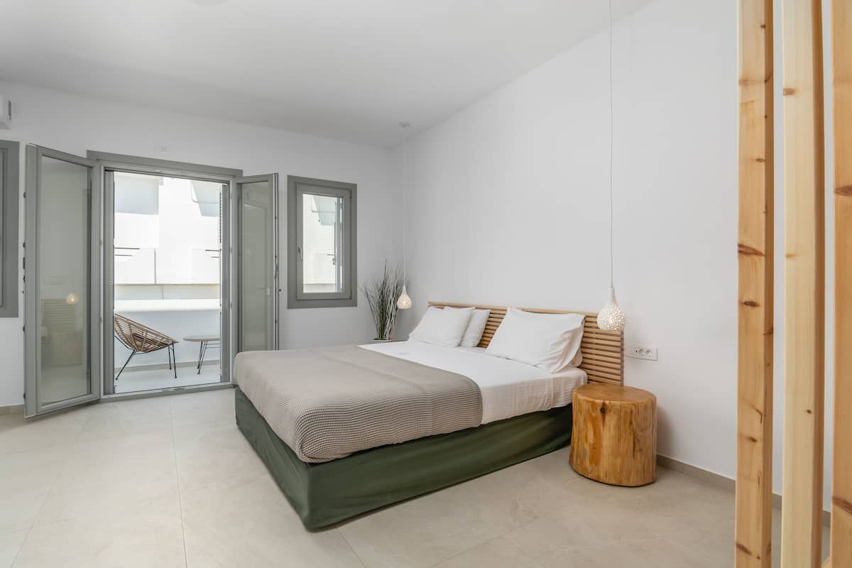 A modern bedroom with a bed, a wooden stool, and a sliding glass door leading to an outdoor area.