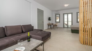 A modern living room with a grey sofa, a wooden coffee table, and a bottle of champagne. There is a TV on a stand, a wooden partition, and a balcony with a view. - Olive Studios (Milos)