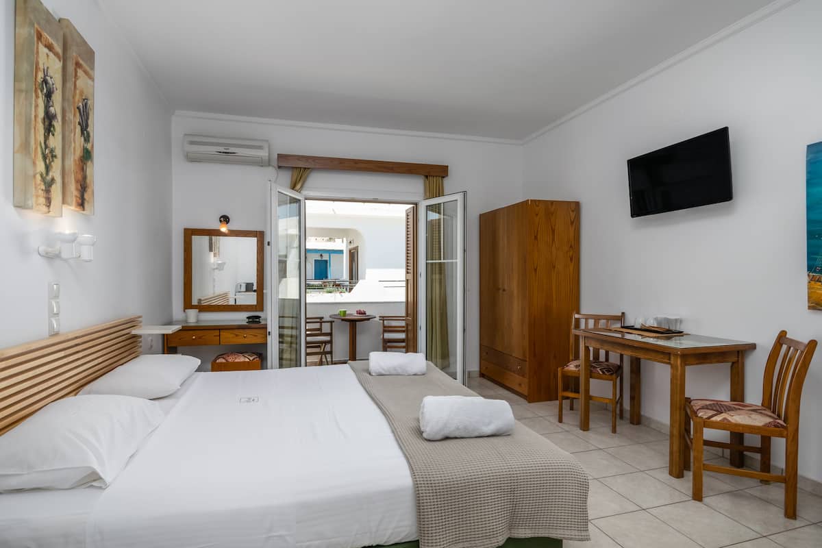 A hotel room with a bed, a desk, a chair, a wardrobe, a TV, and a bathroom visible through an open door.
