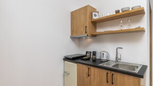 A compact kitchen with wooden cabinets, a black countertop, a stainless steel sink, and a small dishwasher. - Olive Studios (Milos)