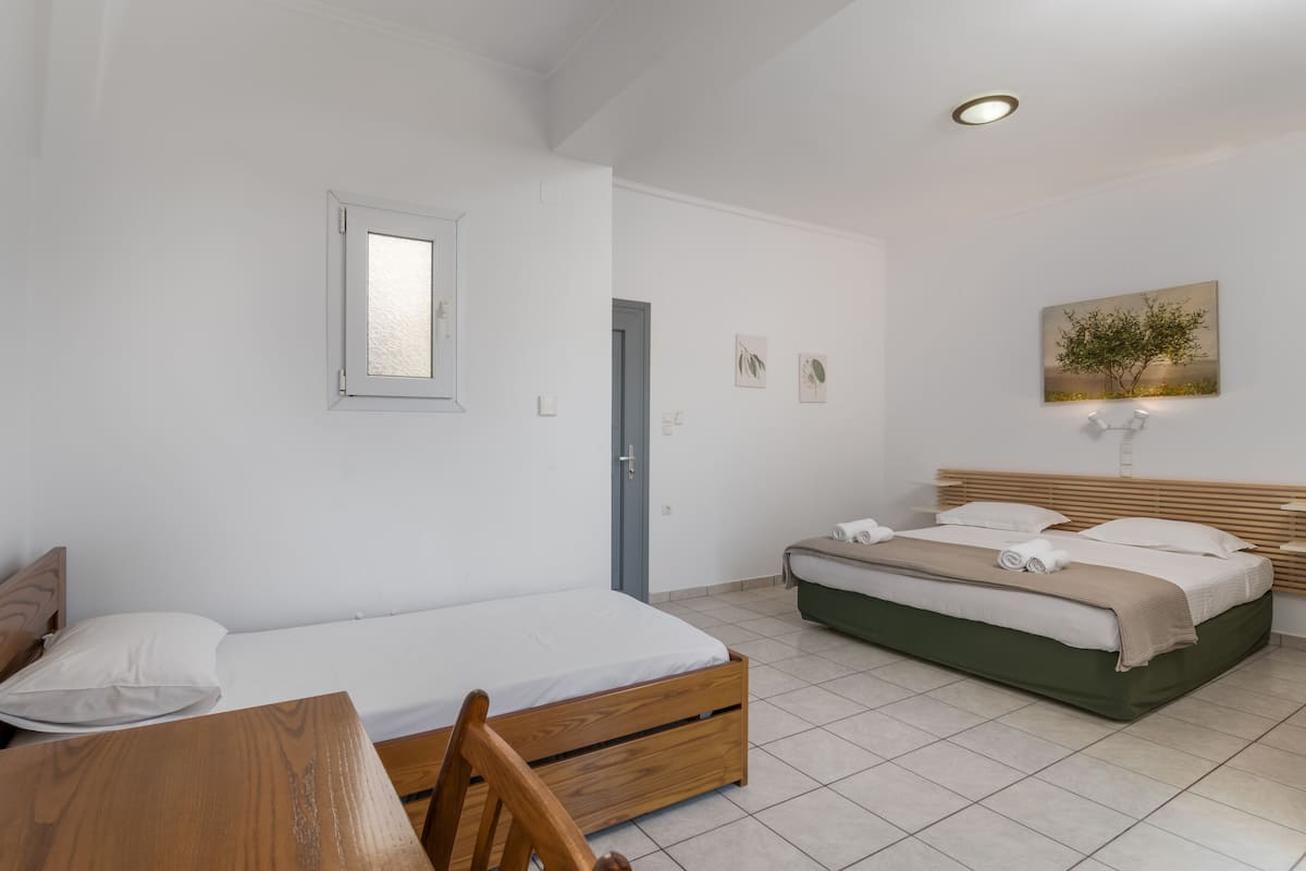 A bedroom with a single bed, a wooden chair, a desk, and a small table.